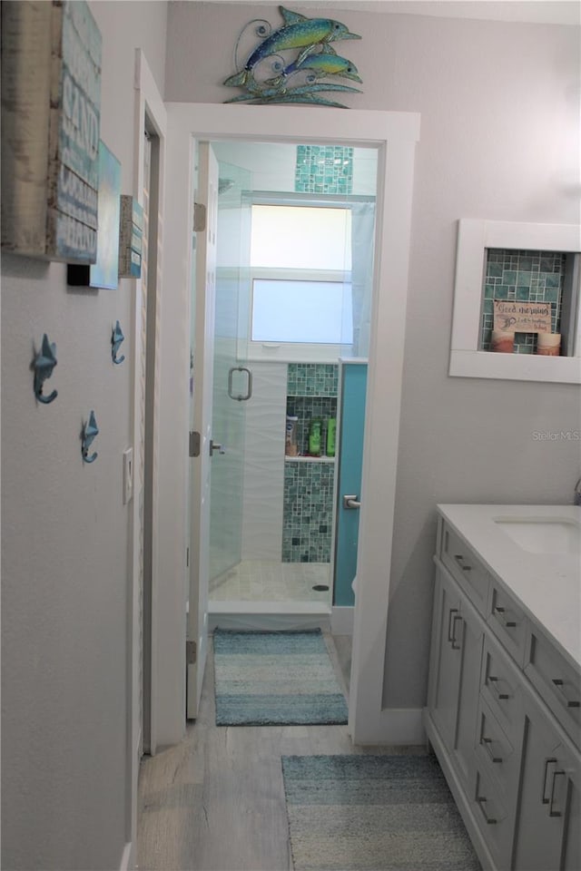 full bath with a stall shower, vanity, baseboards, and wood finished floors