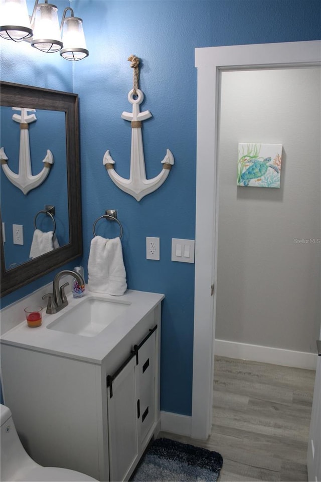 bathroom with toilet, vanity, baseboards, and wood finished floors