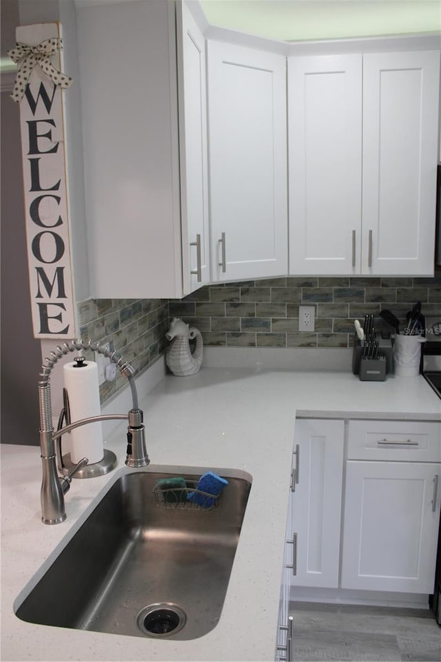 kitchen featuring white cabinetry, a sink, backsplash, and light stone countertops