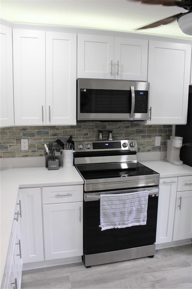 kitchen with appliances with stainless steel finishes, white cabinetry, light wood-style flooring, and decorative backsplash