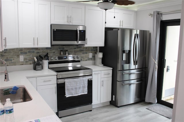 kitchen featuring white cabinets, backsplash, stainless steel appliances, light countertops, and a sink