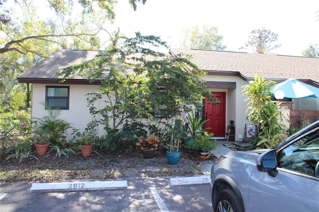 view of front of house with a shingled roof, uncovered parking, and stucco siding