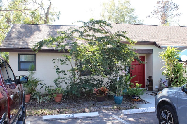 view of front of home featuring stucco siding, uncovered parking, and roof with shingles