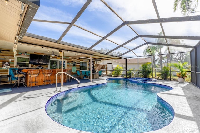 view of swimming pool with glass enclosure, an in ground hot tub, exterior bar, and a patio