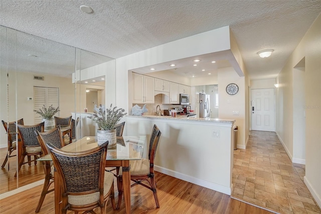 dining space featuring sink, a textured ceiling, and light wood-type flooring