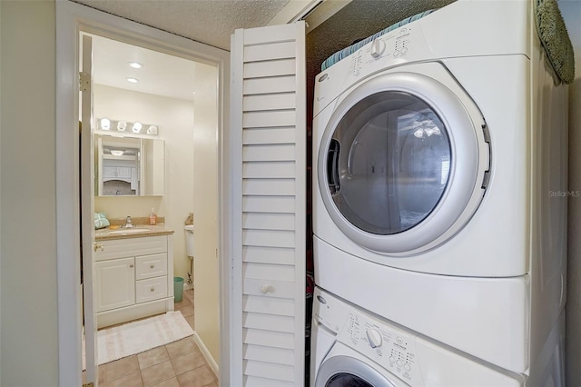 washroom featuring sink, stacked washer and clothes dryer, a textured ceiling, and light tile patterned flooring