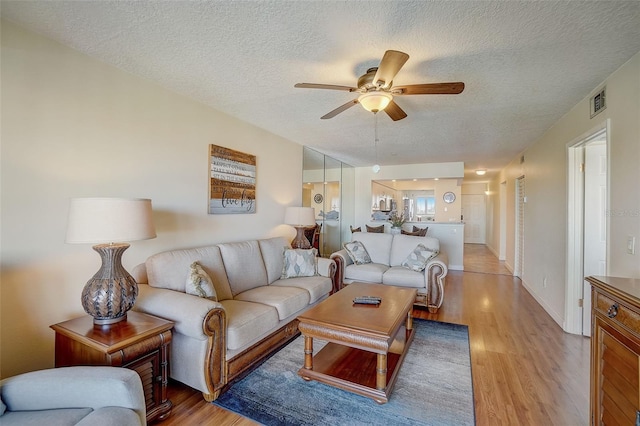 living room with ceiling fan, a textured ceiling, and light hardwood / wood-style floors