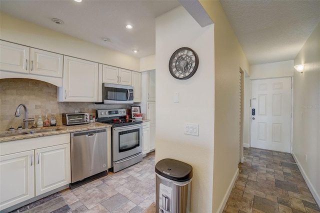 kitchen with sink, white cabinetry, appliances with stainless steel finishes, light stone countertops, and backsplash