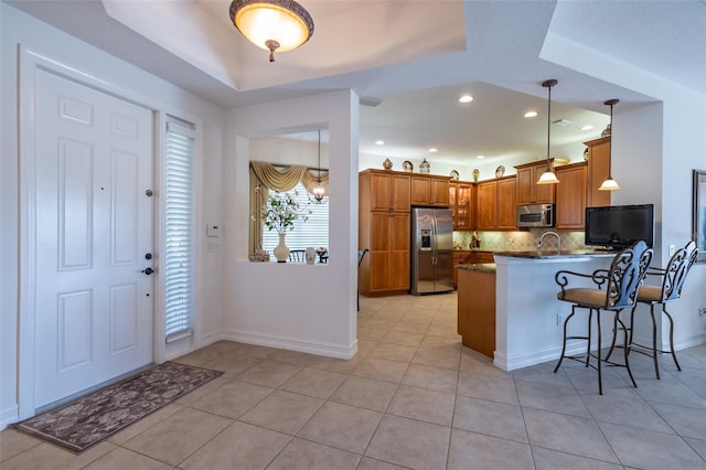 kitchen featuring kitchen peninsula, tasteful backsplash, stainless steel appliances, a raised ceiling, and light tile patterned floors