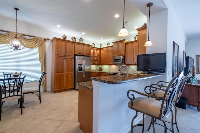 kitchen featuring a breakfast bar, dark stone countertops, appliances with stainless steel finishes, decorative light fixtures, and kitchen peninsula