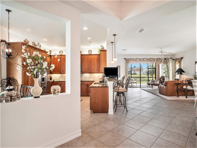 kitchen featuring a kitchen breakfast bar, ceiling fan with notable chandelier, hanging light fixtures, light tile patterned flooring, and kitchen peninsula