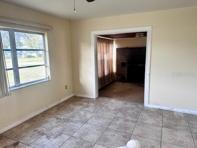 spare room with plenty of natural light, ceiling fan, light tile patterned floors, and a brick fireplace