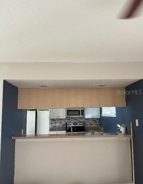 kitchen featuring a textured ceiling, light brown cabinets, stainless steel appliances, and tasteful backsplash