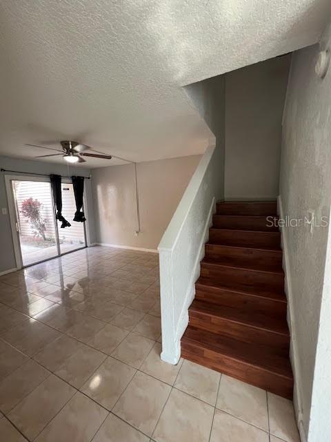 stairs with tile patterned flooring, ceiling fan, and a textured ceiling