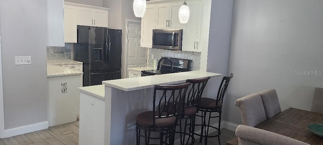 kitchen featuring a kitchen breakfast bar, backsplash, black appliances, white cabinetry, and hanging light fixtures