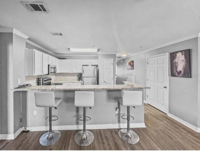 kitchen featuring light stone countertops, appliances with stainless steel finishes, backsplash, a breakfast bar, and white cabinets