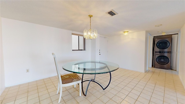 unfurnished dining area with a notable chandelier, light tile patterned floors, and stacked washer and clothes dryer