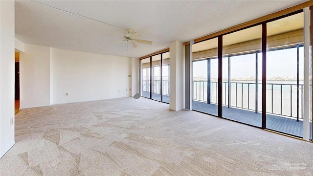 carpeted empty room featuring ceiling fan, a water view, and a wall of windows