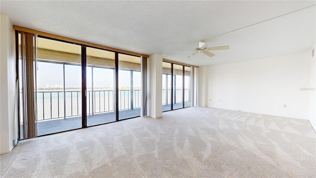 carpeted empty room with a textured ceiling, a water view, a wall of windows, and ceiling fan