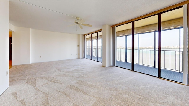 carpeted empty room with floor to ceiling windows, a water view, and ceiling fan