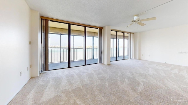 empty room with ceiling fan, expansive windows, a textured ceiling, light carpet, and a water view