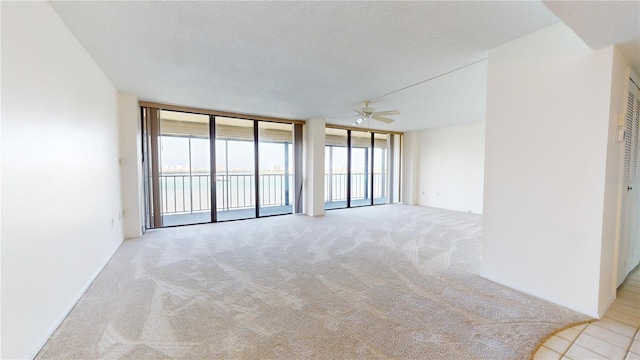 carpeted spare room with a textured ceiling, expansive windows, and ceiling fan