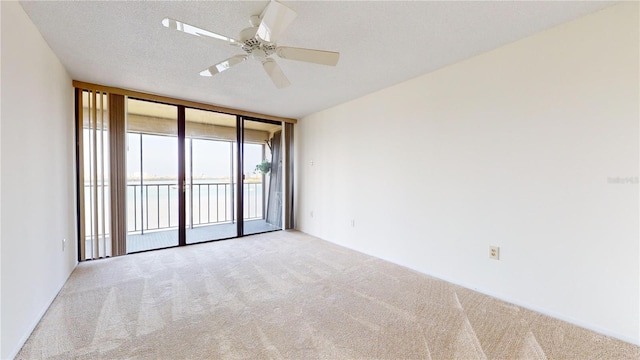 carpeted spare room with a textured ceiling, a wall of windows, and ceiling fan