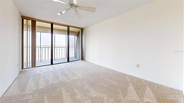 carpeted spare room with ceiling fan, a textured ceiling, and a wall of windows