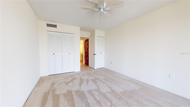 unfurnished bedroom with ceiling fan, light colored carpet, and two closets