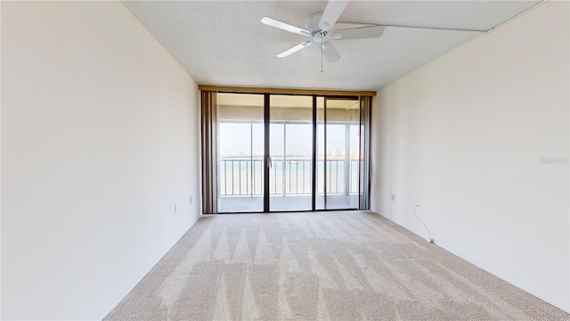 carpeted empty room with ceiling fan, expansive windows, a water view, and a textured ceiling