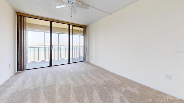 empty room with floor to ceiling windows, a water view, ceiling fan, a textured ceiling, and light colored carpet