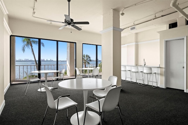 carpeted dining space with a water view, track lighting, and ceiling fan