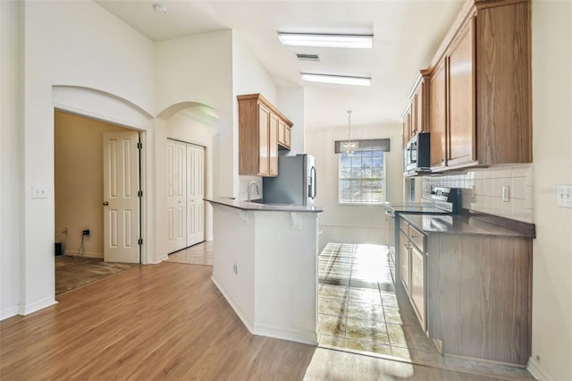 kitchen featuring decorative backsplash, stainless steel appliances, light hardwood / wood-style flooring, and hanging light fixtures