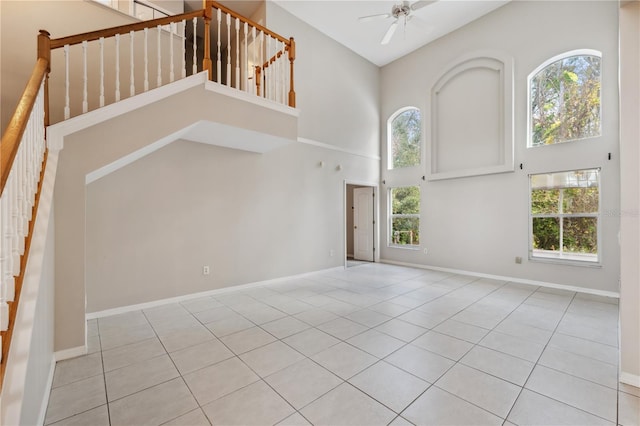 unfurnished living room with ceiling fan, light tile patterned flooring, a healthy amount of sunlight, and a high ceiling