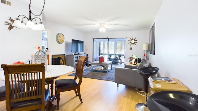 dining space with ceiling fan with notable chandelier and light wood-type flooring