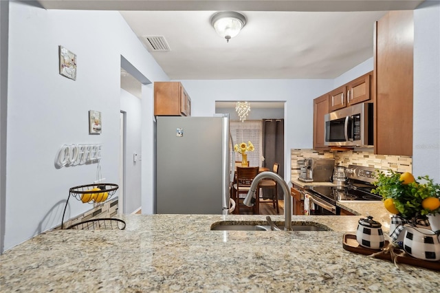 kitchen featuring appliances with stainless steel finishes, backsplash, a notable chandelier, light stone countertops, and sink