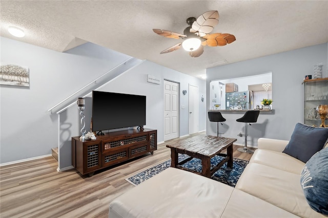 living room with a textured ceiling, ceiling fan, and light wood-type flooring