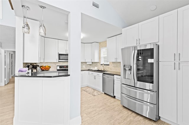 kitchen with sink, hanging light fixtures, vaulted ceiling, white cabinets, and appliances with stainless steel finishes