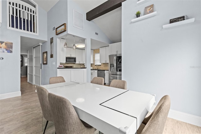 dining area with beam ceiling, light hardwood / wood-style floors, and high vaulted ceiling