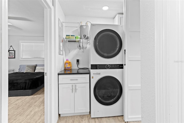 laundry area featuring light hardwood / wood-style flooring, cabinets, and stacked washer / drying machine