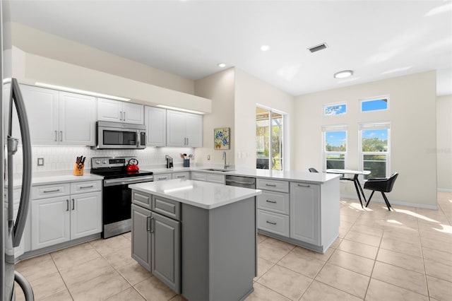 kitchen with kitchen peninsula, decorative backsplash, stainless steel appliances, sink, and a center island