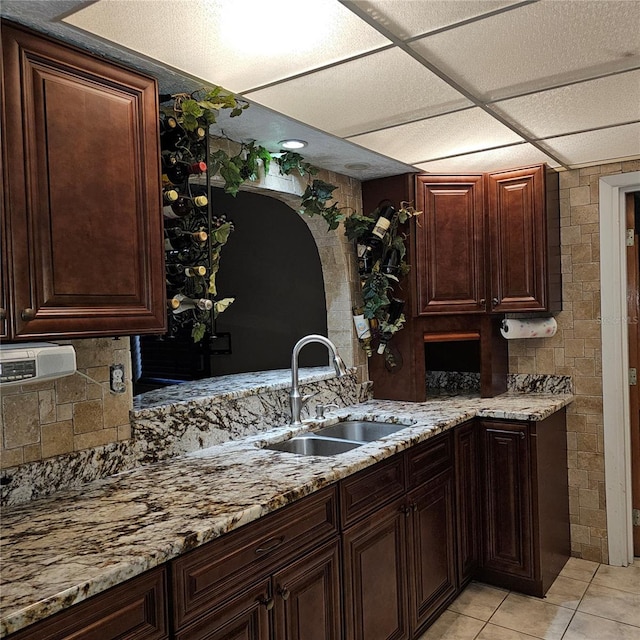 kitchen with light stone countertops, light tile patterned floors, a paneled ceiling, and sink