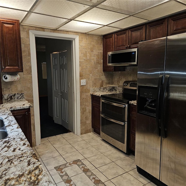 kitchen featuring dark brown cabinetry, light stone countertops, light tile patterned floors, and stainless steel appliances