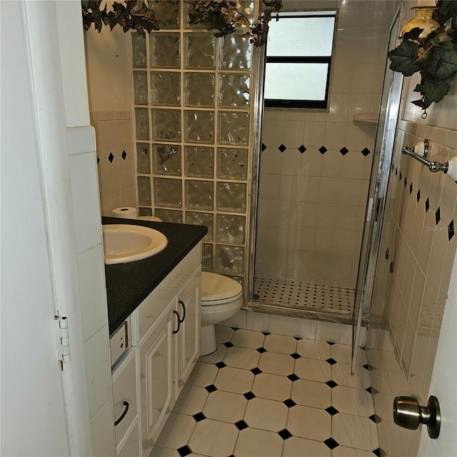 bathroom with a shower with door, vanity, tile walls, and toilet