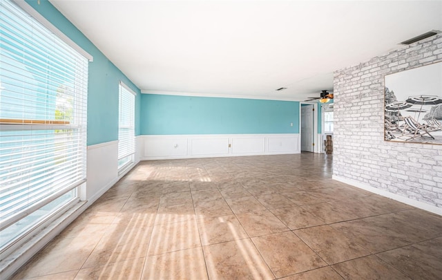 tiled spare room with ceiling fan and brick wall