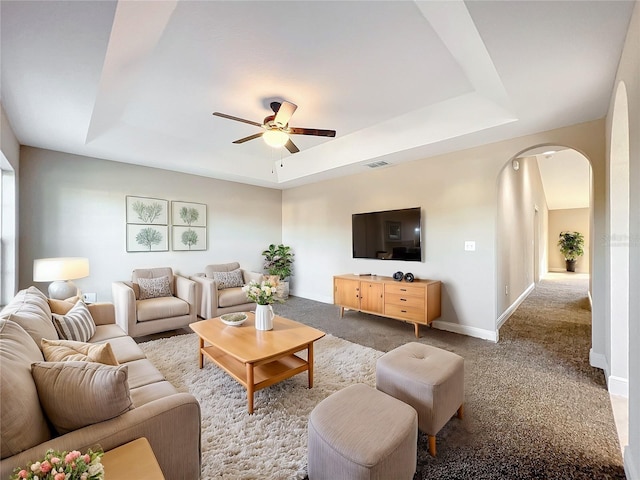 living room featuring a raised ceiling, light carpet, and ceiling fan