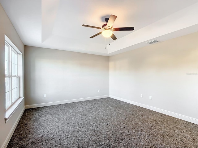 carpeted spare room featuring a raised ceiling, a wealth of natural light, and ceiling fan