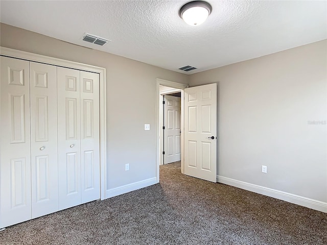 unfurnished bedroom with a textured ceiling, dark carpet, and a closet