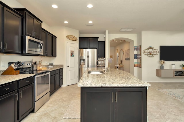 kitchen with light stone countertops, stainless steel appliances, a kitchen island with sink, and sink