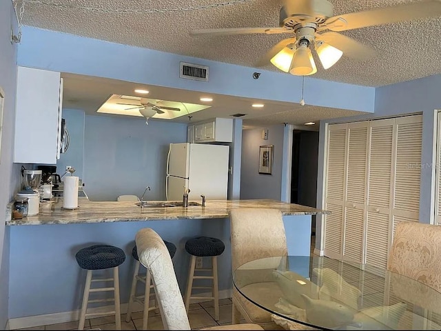 kitchen with kitchen peninsula, sink, white cabinets, and white fridge